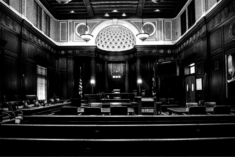 The interior of an empty United States courtroom, in high contrast black and white with coarse grain