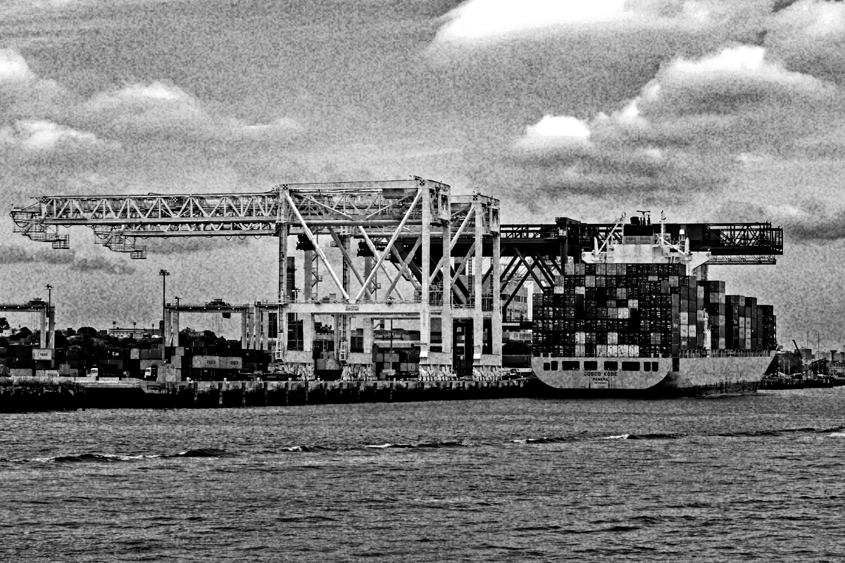 A container ship at a terminal with gantry cranes, in high contrast black and white with coarse grain