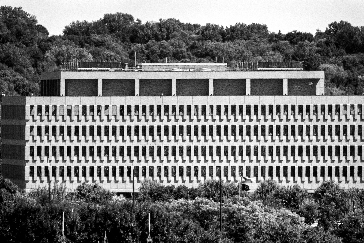 The Bishop Henry Whipple Federal Building near Fort Snelling, Minnesota, a long concrete block with rows of narrow windows above a band of trees, wooded hills behind, in grainy high-contrast black and white