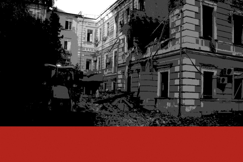 A loader clearing rubble beside the damaged facade of the Presidium of the National Academy of Sciences of Ukraine in Kyiv, its upper floors torn open, in near black and white with a flat red band along the foot of the frame