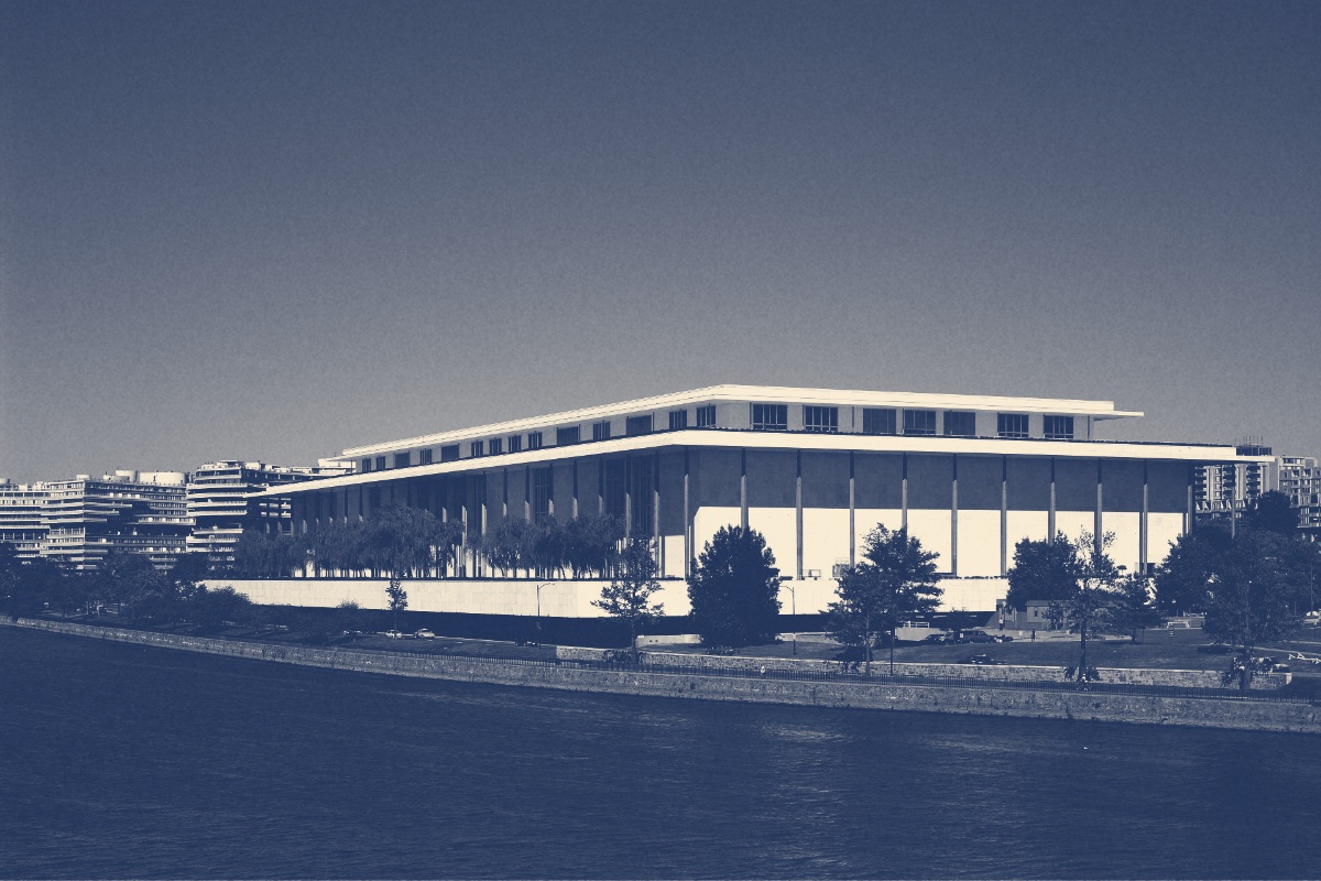 The Kennedy Center seen from across the Potomac, a long white colonnaded building beside the water, in a slate and bone duotone