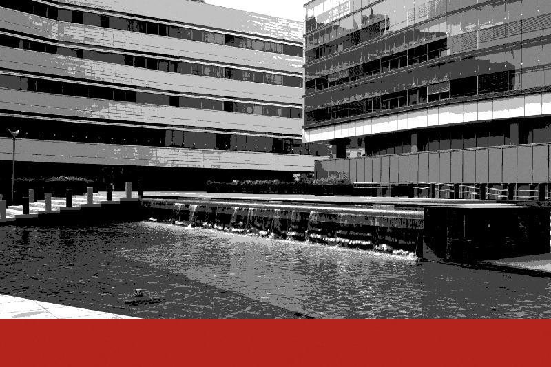 The courtyard of the Parliamentary Assembly building in Sarajevo, banded stone and glass office blocks above a shallow pool with a low cascade, in near black and white with a flat red band along the foot of the frame