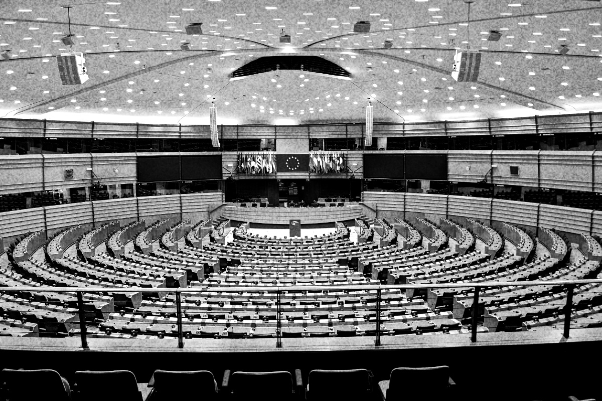 The curved tiered seating of the European Parliament chamber in Brussels, empty, seen from the upper gallery, in high-contrast black and white with visible grain