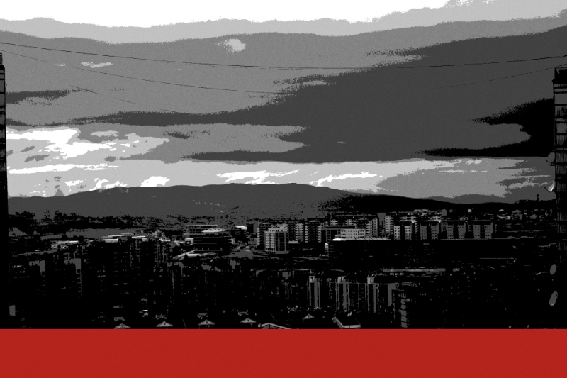 A view across the rooftops and tower blocks of Pristina from a hillside, in near black and white with a red bar along the foot