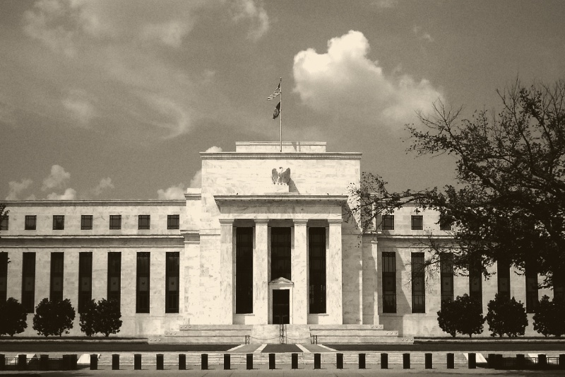 The Marriner S. Eccles Federal Reserve Board Building in Washington, its white marble facade and eagle above the entrance, a flag on the roof, in an ink and bone duotone