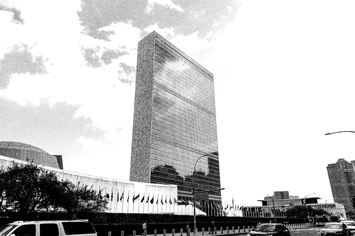 The United Nations Secretariat building in New York seen from First Avenue, with member-state flagpoles and security bollards in the foreground, in high contrast black and white with coarse grain