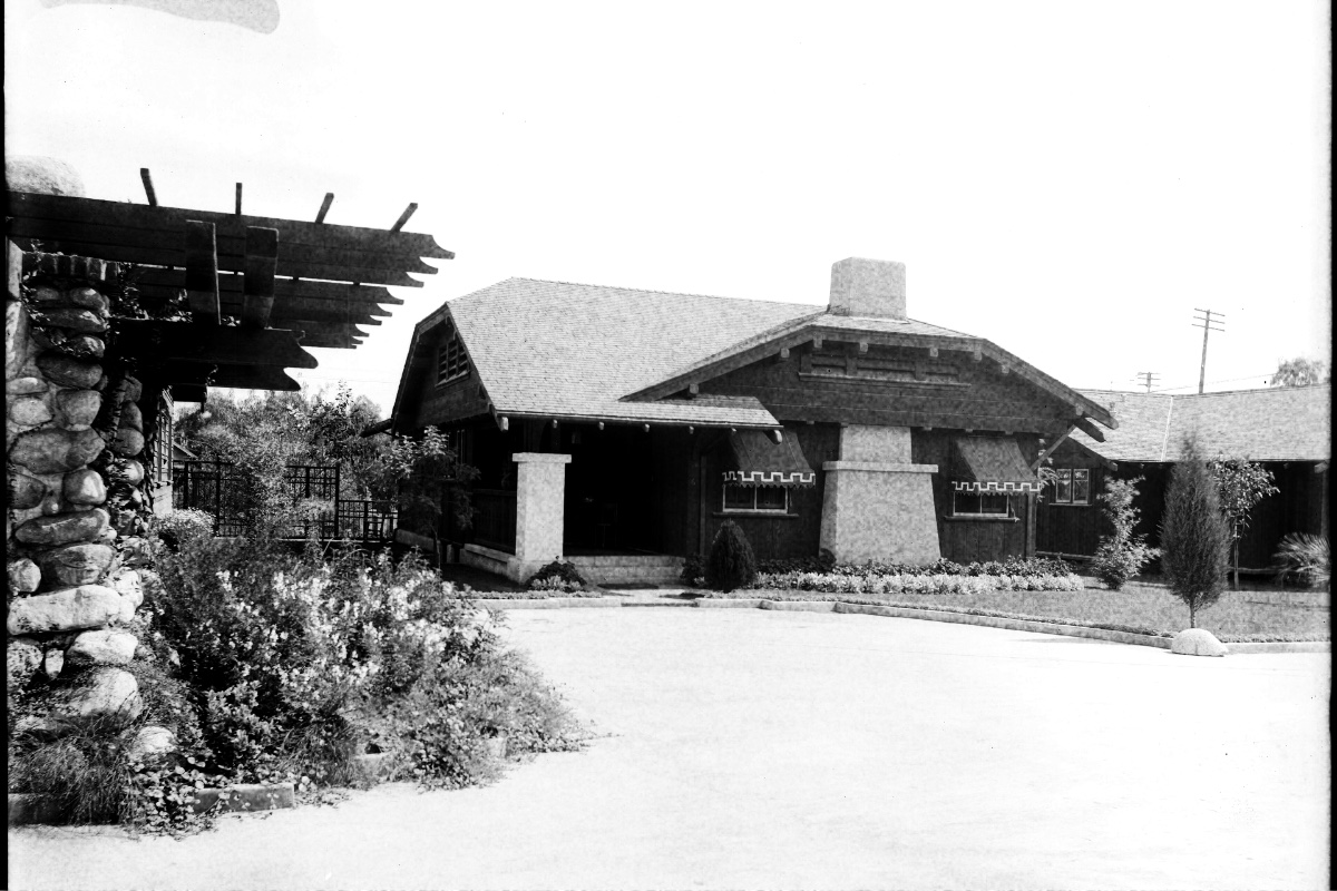 A single-storey California bungalow with a deep shaded porch and low-pitched roof, photographed in Pasadena in 1916, in high-contrast black and white with visible grain
