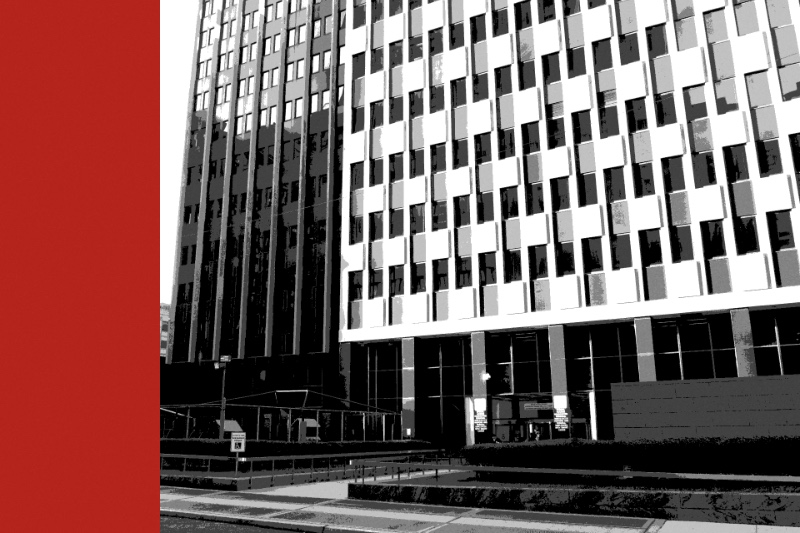 The facade of the Jacob K. Javits Federal Building at 26 Federal Plaza in Manhattan, a dark tower beside it, in near black and white with a flat red bar down the left edge of the frame