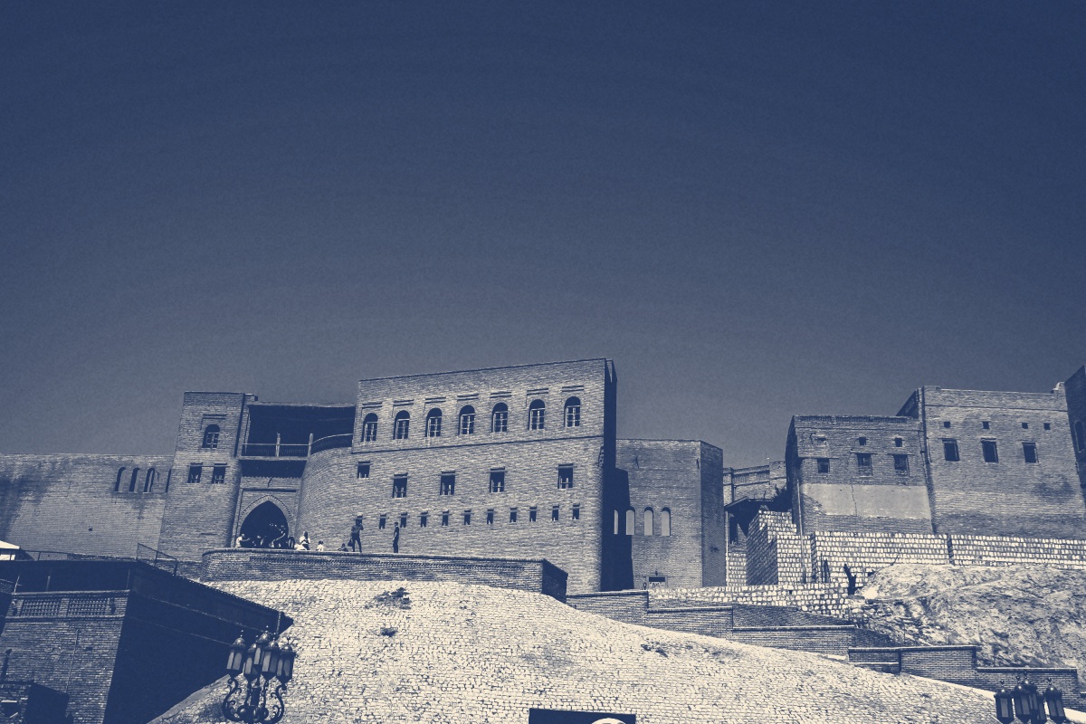 The brick walls and arched gateway of the Erbil citadel on its mound under a clear sky, in a slate and bone duotone