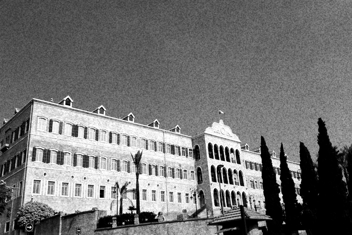 The Grand Serail in Beirut, the seat of the prime minister, a long three-storey Ottoman-era building with rows of arched windows and a tiled roof, palm trees and tall cypresses in front against an empty sky, in grainy high-contrast black and white