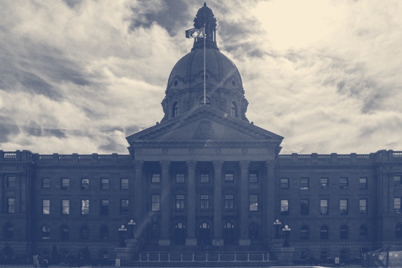 The Alberta Legislature Building in Edmonton, a stone building with a central dome and a columned entrance under a bright cloudy sky, in a slate and bone duotone