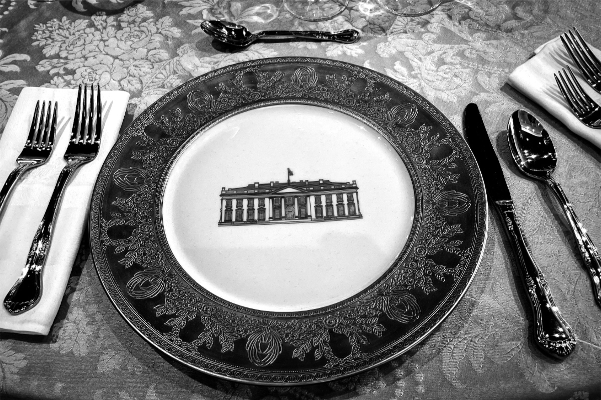 A place setting at a formal dinner, the service plate embossed with the north front of the White House, in black and white