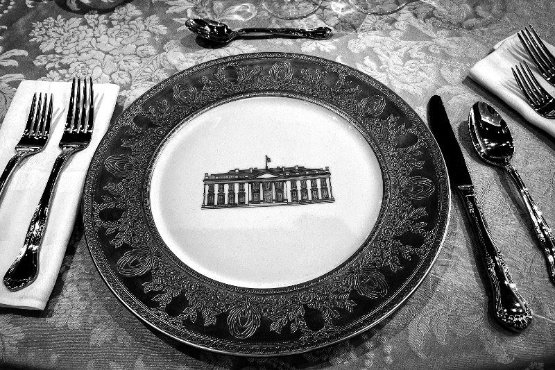 A place setting at a formal dinner, the service plate embossed with the north front of the White House, in black and white