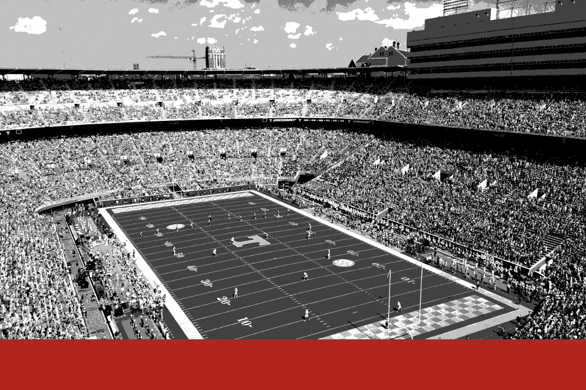 A college football stadium seen from high in the stands, the field ringed by tens of thousands of spectators, in near black and white with a flat red band along the foot of the frame