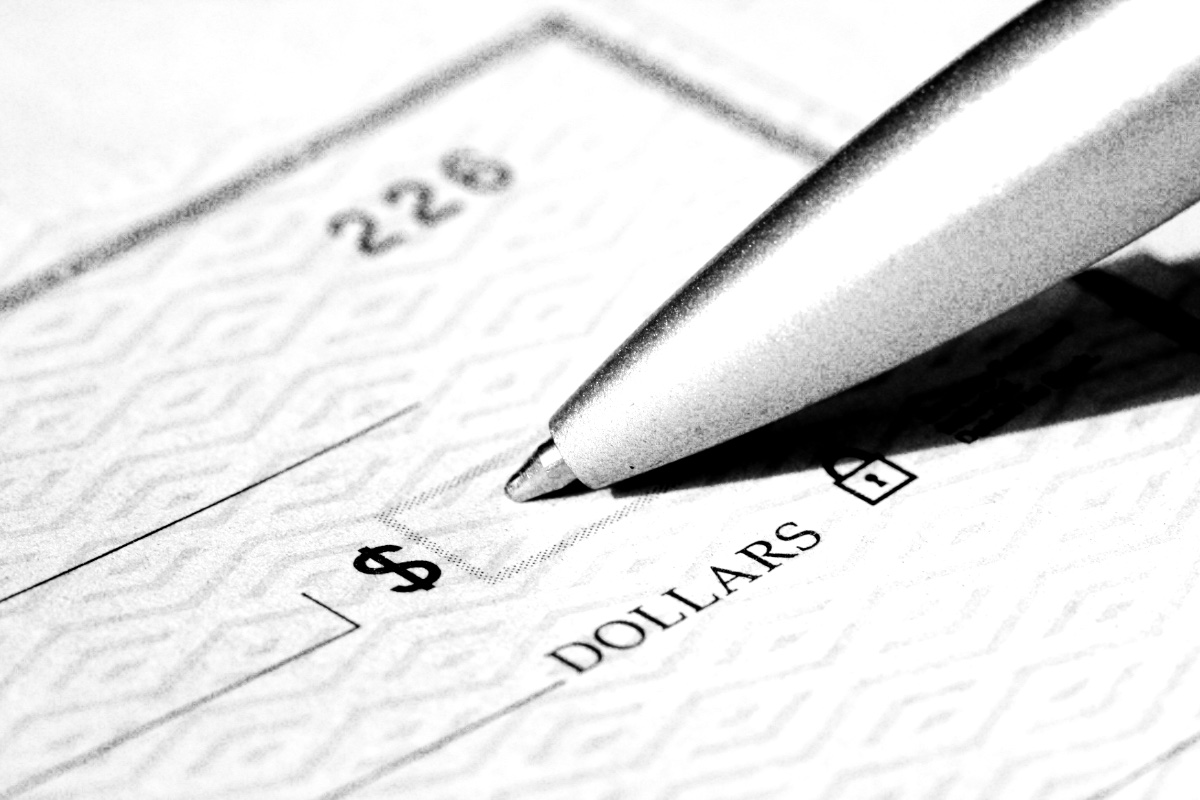 A silver pen poised over the amount line of a blank cheque, in high contrast black and white with coarse grain