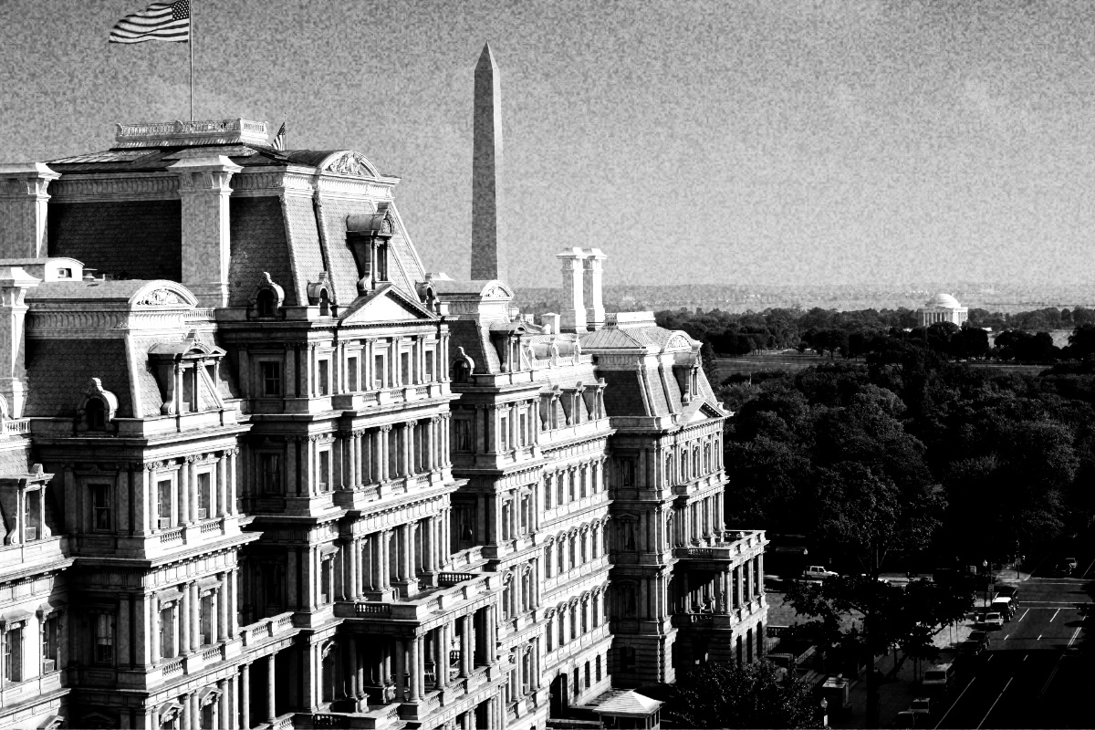 The mansard roofs and columned facades of the Eisenhower Executive Office Building seen from above, the Washington Monument and Jefferson Memorial beyond, in high contrast black and white with coarse grain