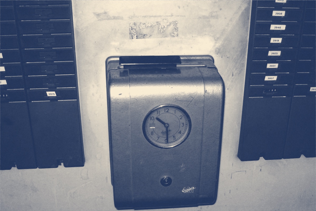 A wall-mounted time recorder clock flanked by racks of numbered time cards