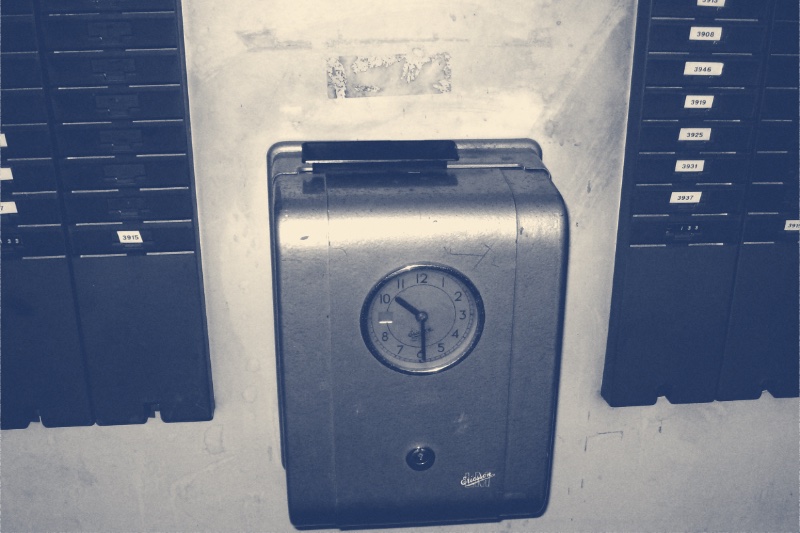A wall-mounted time recorder clock flanked by racks of numbered time cards