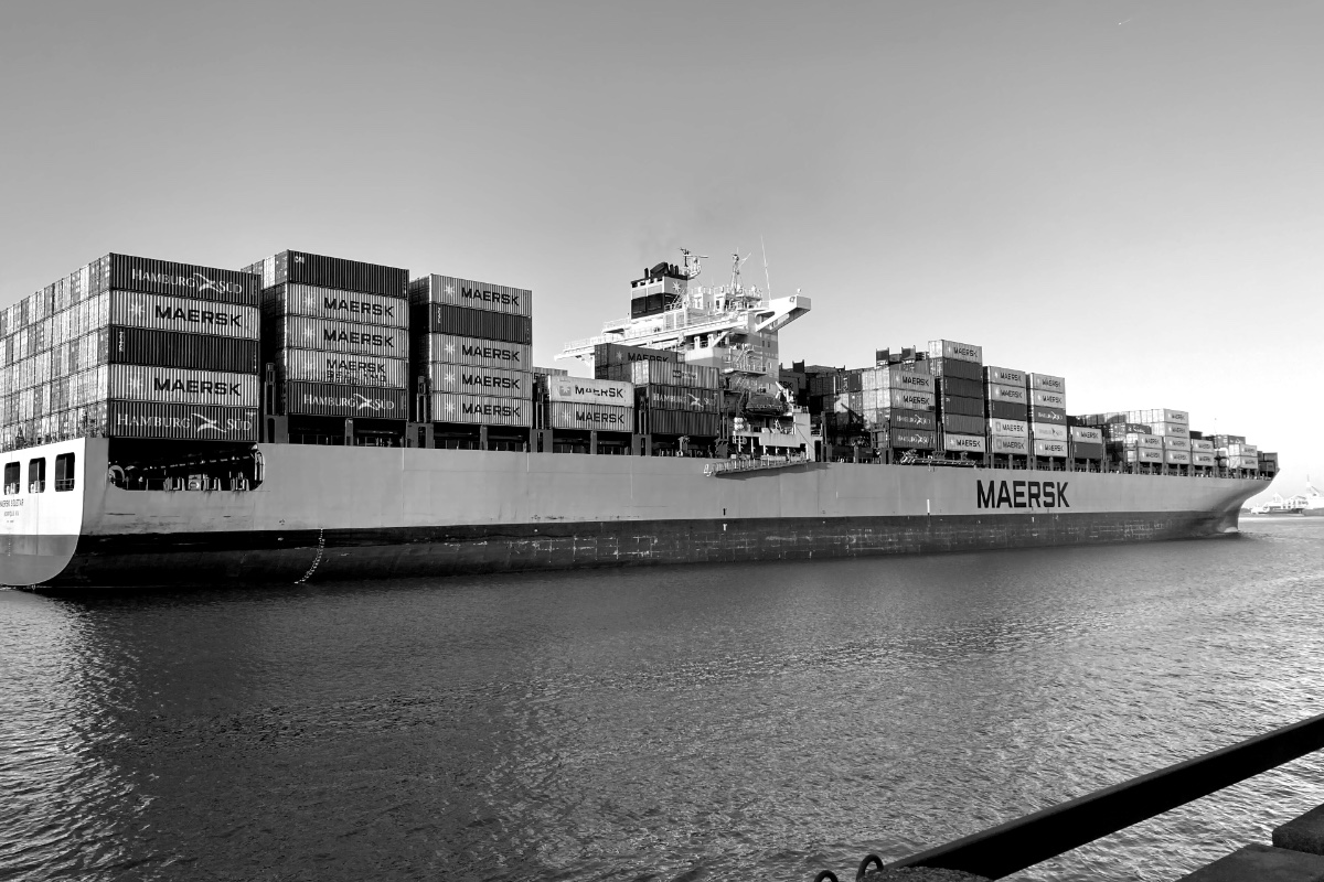 The container ship Maersk Seletar under way on the Savannah River, its hull and stacked containers marked Maersk, seen from a waterfront railing in low sun