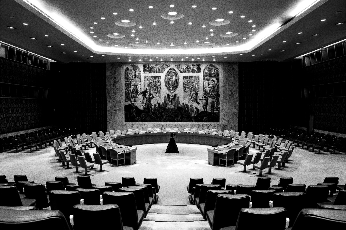 The empty Security Council chamber at UN headquarters in New York, its horseshoe table and rows of seats facing the large mural on the far wall, in high contrast black and white with coarse grain