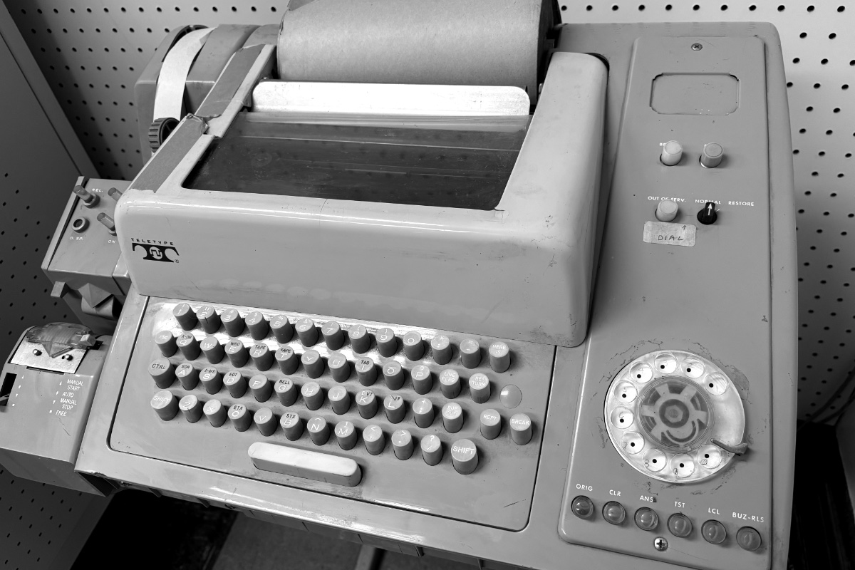 A mid-century teleprinter with a keyboard and dial, in plain black and white