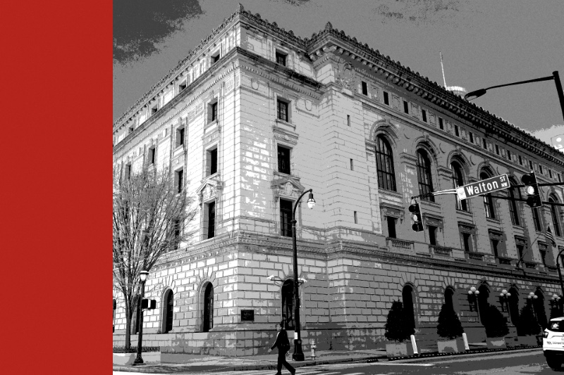 The Elbert P. Tuttle Court of Appeals Building in Atlanta, a granite Renaissance Revival block on a street corner with arched windows, a street lamp and traffic lights, and a pedestrian crossing in front, in near black and white with a flat red band down the left edge